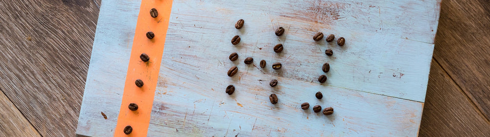 Coffee beans arranged to spell "love" on a wooden board with a strip of orange fabric on the left side in Perth.