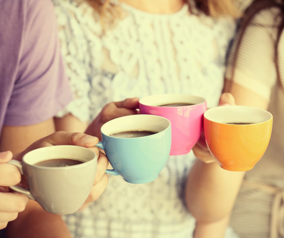 Four people in Perth holding colorful coffee cups in a toast-like gesture, with a focus on the cups. the background is softly blurred, highlighting the interaction and cheerful moment.